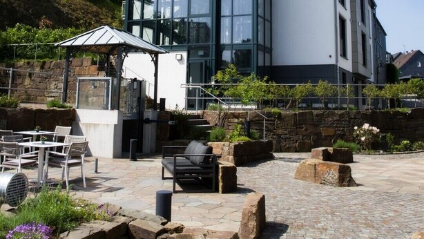 A modern building with a glass facade, outdoor seating area, and stone planters. - Hotel am Markt (Wipperfuerth)