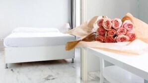 Ein Zimmer mit einem Bett, einem Schreibtisch mit einem Strauß rosa Rosen, einer Lampe und einer Pendelleuchte.