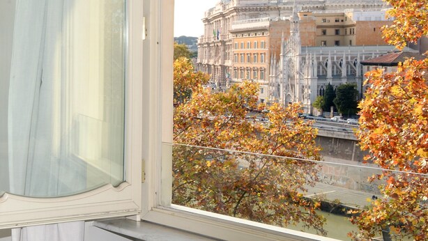 Blick durch ein Fenster mit Vorhang, zeigt ein historisches Gebäude mit aufwendiger Architektur und Herbstlaub.