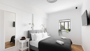 A modern bedroom with a bed, bedside table, and a large mirror. - Spacious & Modern 3BD Apartment 2-min From Beach (Tel Aviv)