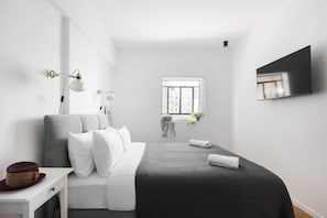 A modern bedroom with a bed, bedside table, lamp, and a TV mounted on the wall.