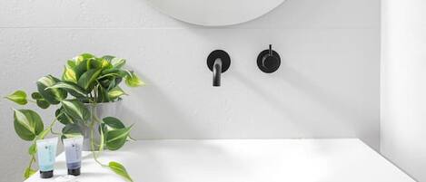 Un baño con lavamanos blanco, tocador de madera, espejo redondo y una planta en maceta.