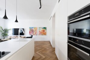 A modern kitchen with a white island, black pendant lights, and a built-in oven.