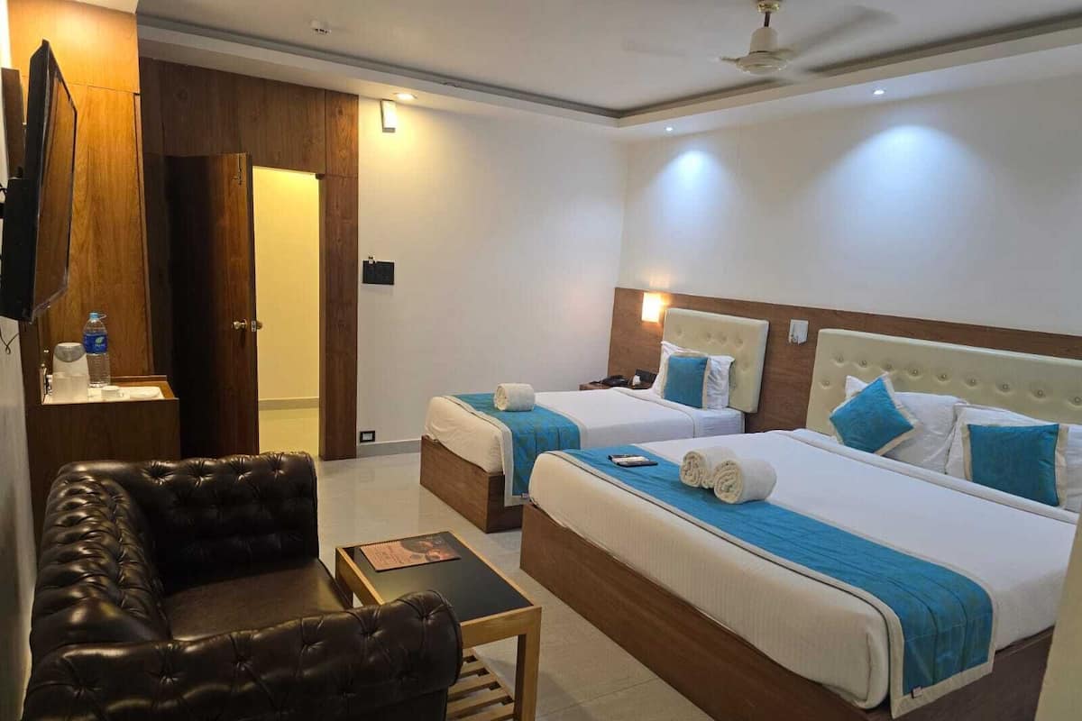 A hotel room with two beds, a leather sofa, a small table, and a TV mounted on the wall.