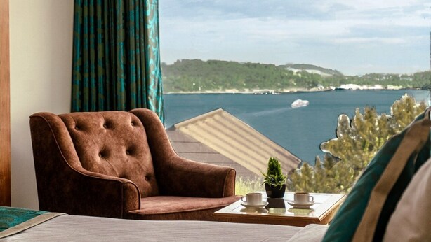 A room with a view of a body of water, a brown armchair, a small table with a cup and a plant. - Hotel De Pebbles (Port Blair)