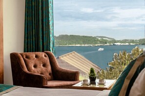A room with a view of a body of water, a brown armchair, a small table with a cup and a plant. - Hotel De Pebbles (Port Blair)