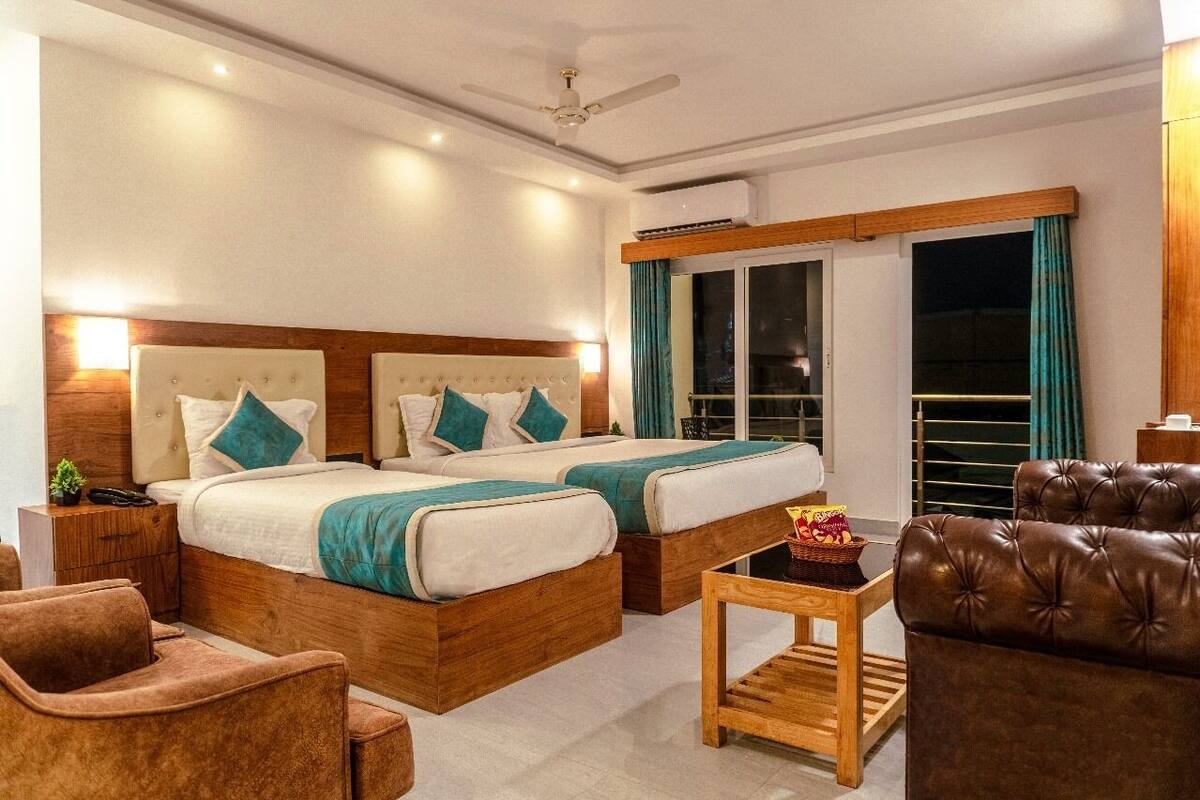 A hotel room with two beds, a ceiling fan, a wooden headboard, a small table with a basket, and a brown leather chair.