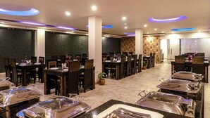 A spacious dining area with multiple tables and chairs, a buffet setup, and a decorative wall. - Hotel De Pebbles (Port Blair)