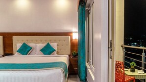 A hotel room with a bed, a nightstand, a small table with a plant, and a balcony with a chair. - Hotel De Pebbles (Port Blair)