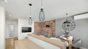 Una cocina moderna con una isla central, luces colgantes, un muro decorativo de ladrillo y un comedor con un reloj.