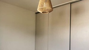 A minimalist bedroom with a bed, a hanging light fixture, and a wardrobe.