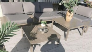 A modern outdoor seating area with a sofa and two tables, one with a decorative plant.