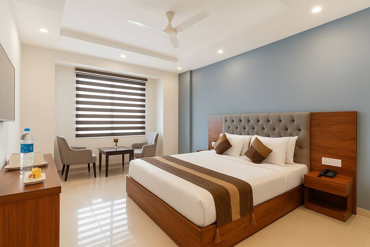 A hotel room with a large bed, a desk, a chair, a small table, and a window with blinds.