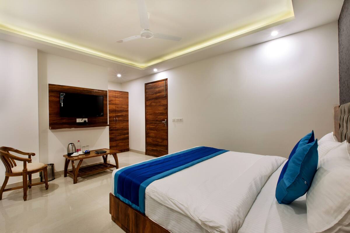 A hotel room with a bed, a TV mounted on the wall, a wooden desk, and a chair.