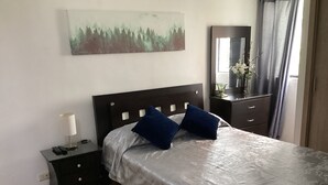 Une chambre à coucher bien rangée, avec un lit, une table de chevet, une lampe, une commode et un tableau au mur.