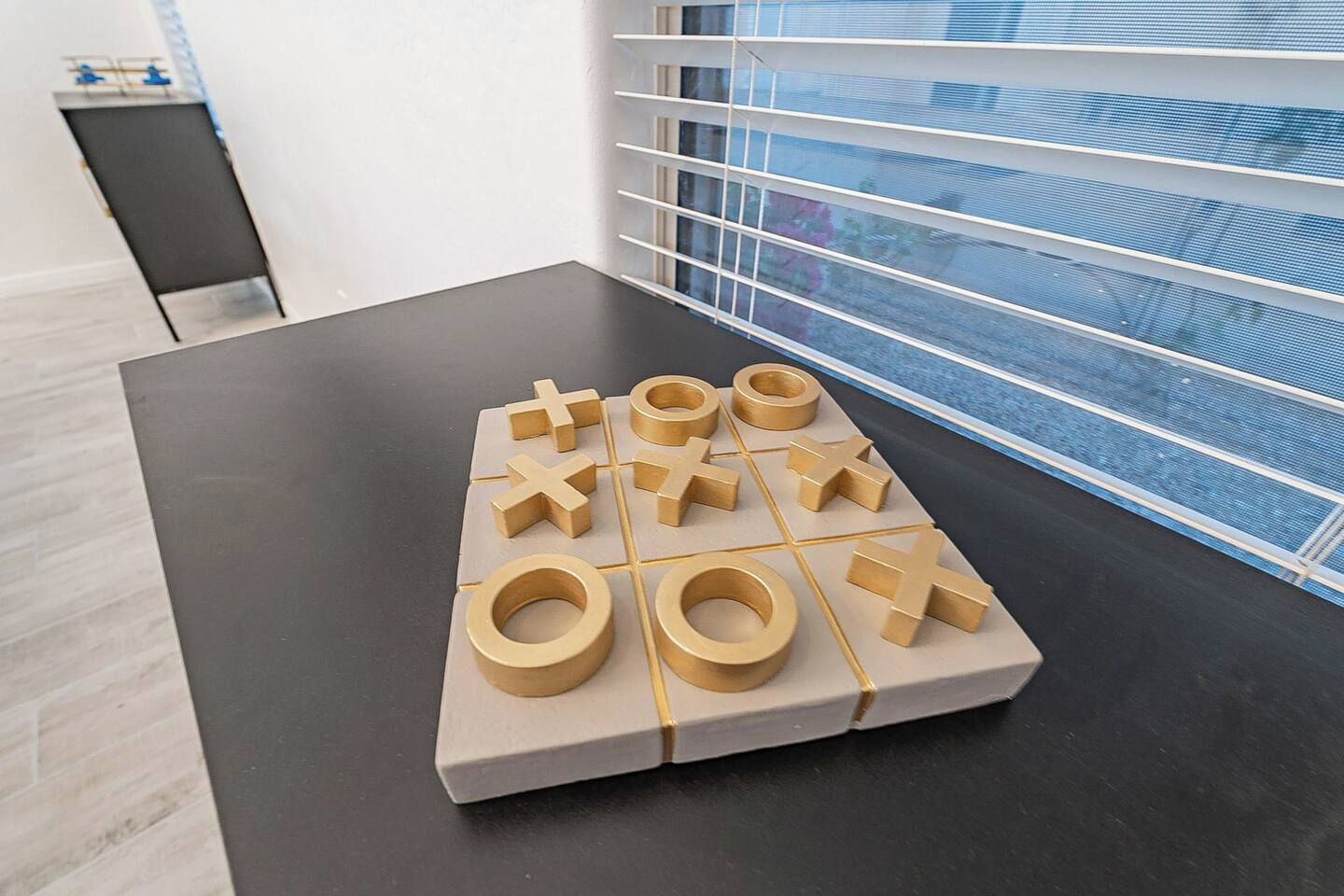 Un juego de tres en raya sobre una mesa en una habitación con ventana y persianas.