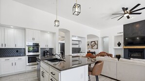 Una cocina moderna con armarios blancos, una isla central y un comedor con sofá y sillas blancos.