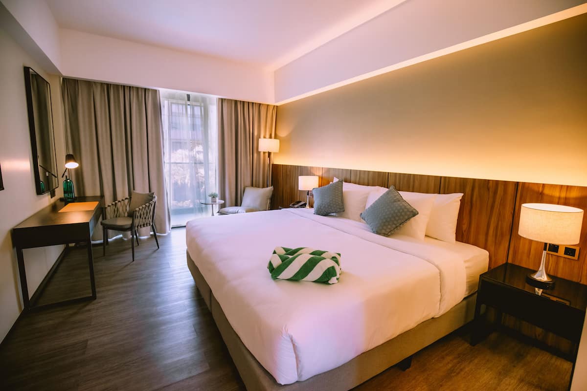 Habitación de hotel con una cama grande, un escritorio, una silla y una mesita de noche con lámpara.