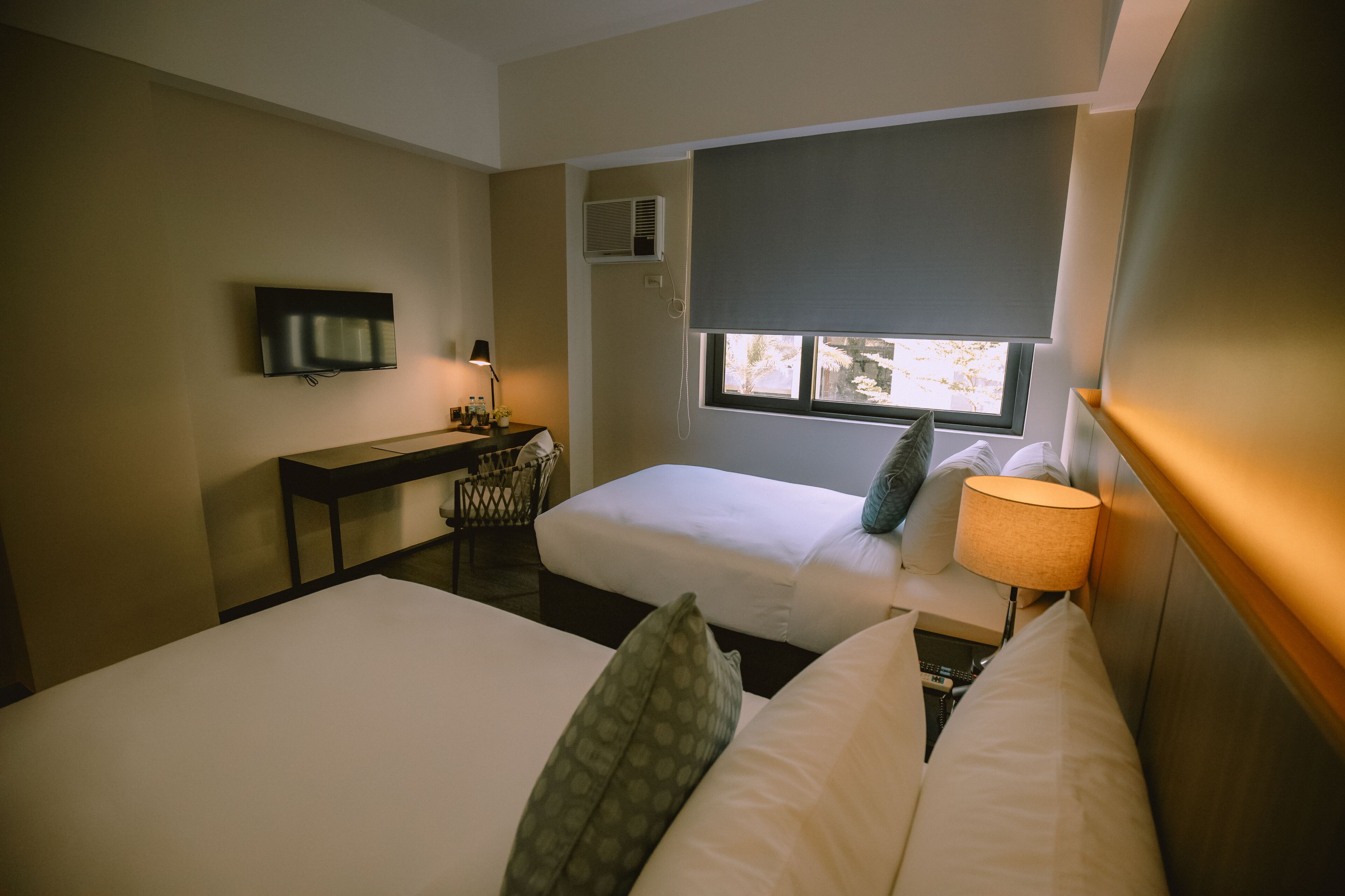 Une chambre d’hôtel avec deux lits, un bureau, une télévision et une fenêtre donnant sur des arbres.