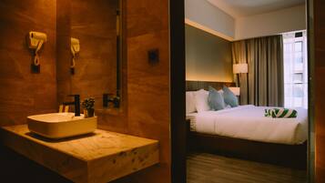 Una habitación de hotel con lavamanos de mármol, cama con ropa blanca, mesita de noche y lámpara.
