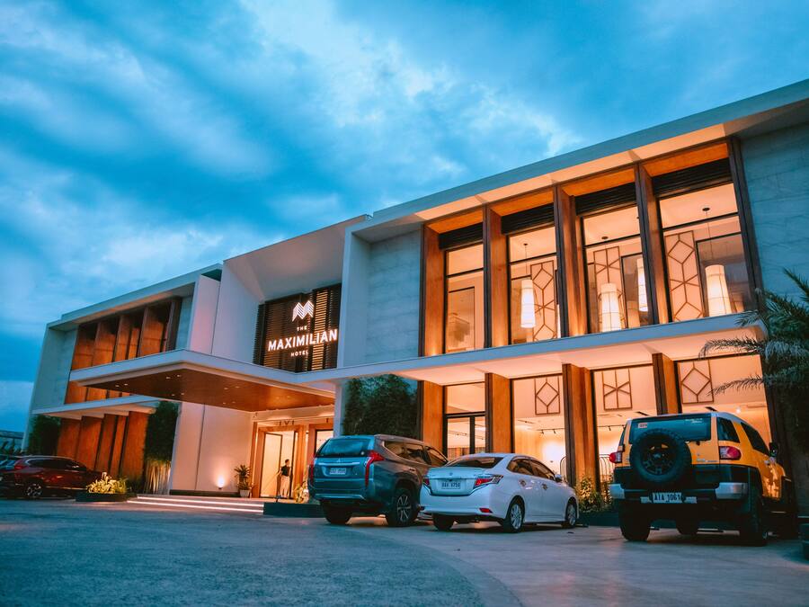 A modern hotel with a prominent sign, two SUVs parked in front, and a well-lit entrance.