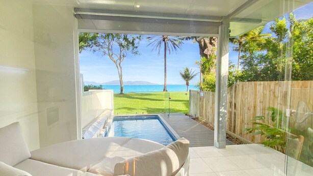 A modern room with a glass wall, a pool, and a view of the sea.