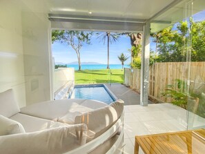 Una habitación moderna con pared de vidrio, piscina y vista al mar.