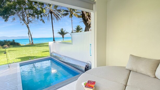 Un espace aménagé au bord de la piscine, avec vue sur l’océan, comprenant un canapé et un livre.