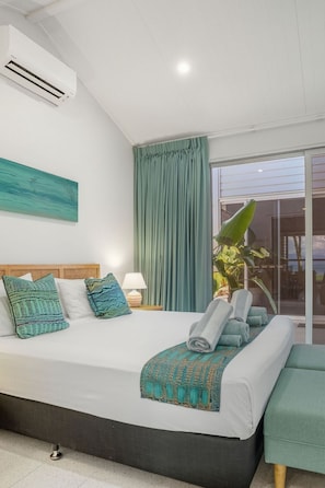 Una habitación de hotel moderna con una cama grande, un ventanal con cortinas, un ventilador de techo y vistas al exterior.
