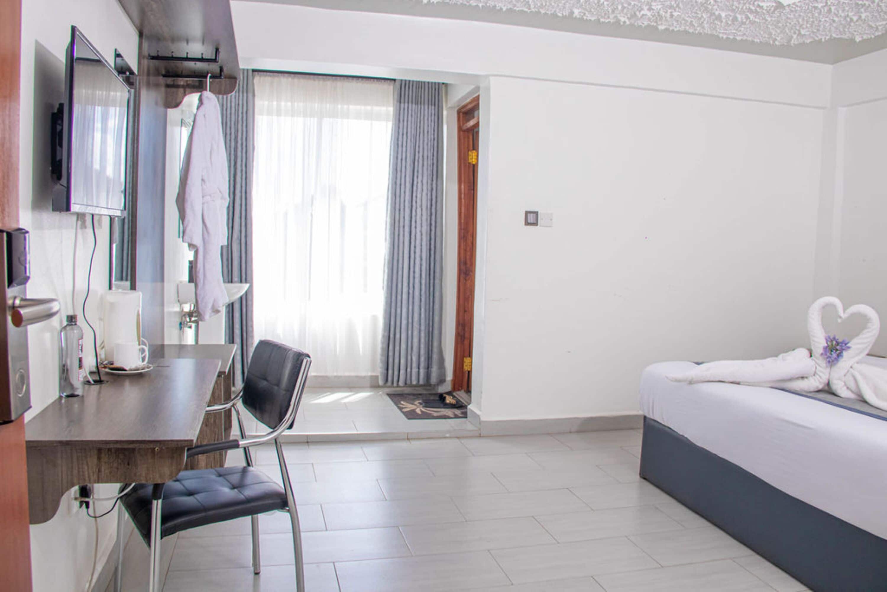 A hotel room with a bed, a desk, a chair, a TV, and a bathroom visible through a door.