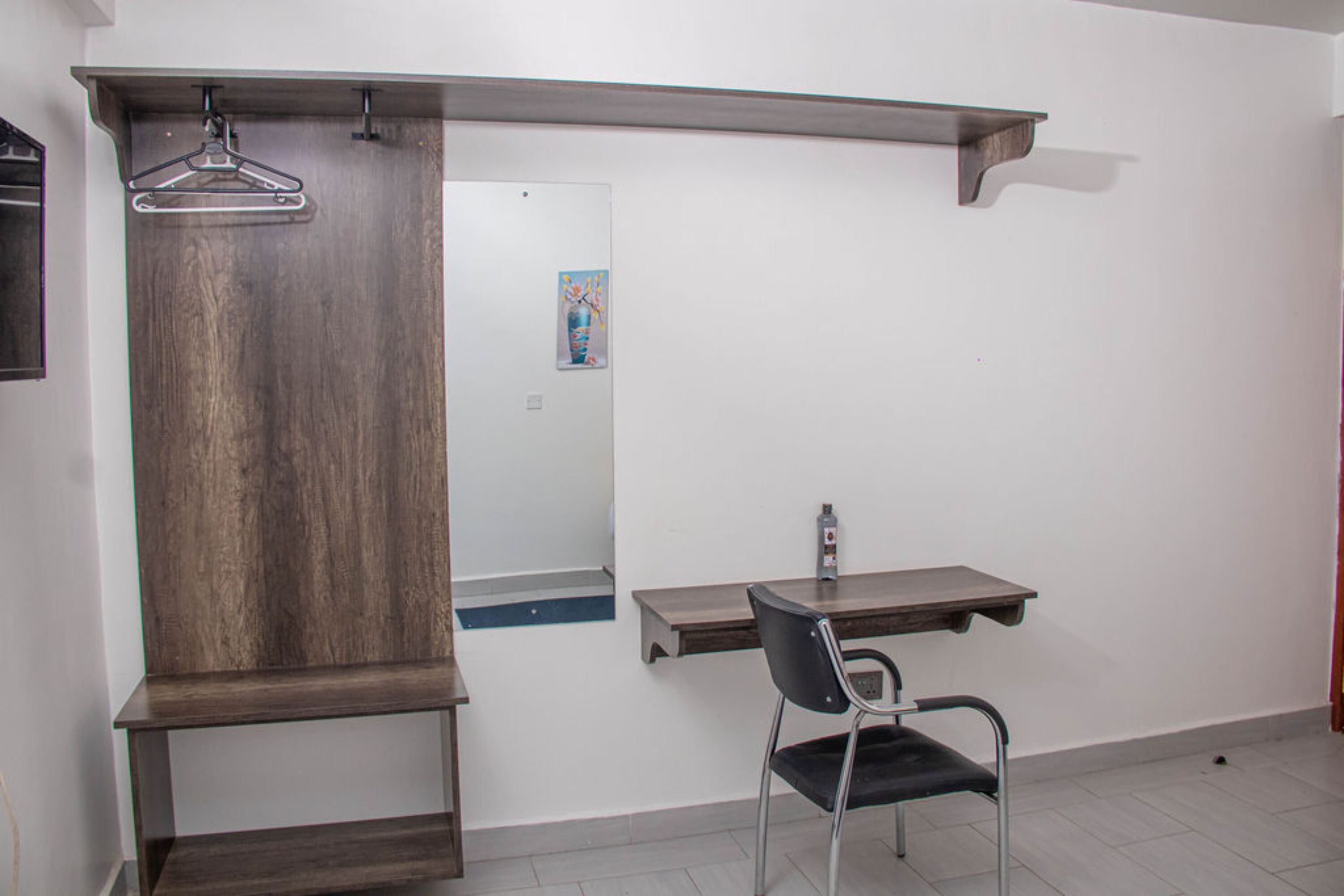 Quarto com guarda-roupa de madeira, espelho, escrivaninha com cadeira e um cabideiro.
