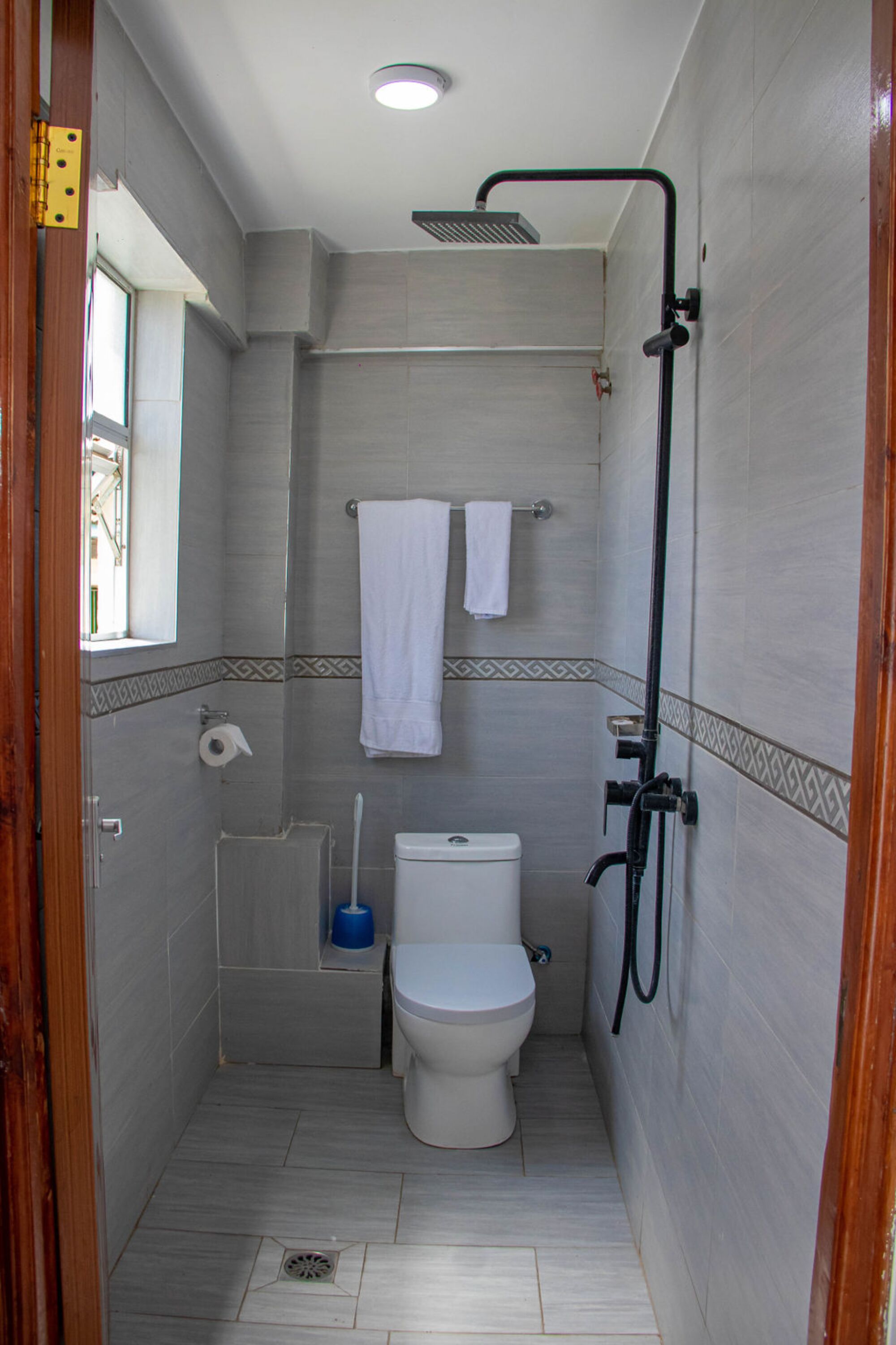 A compact bathroom with a toilet, a shower, and a window.