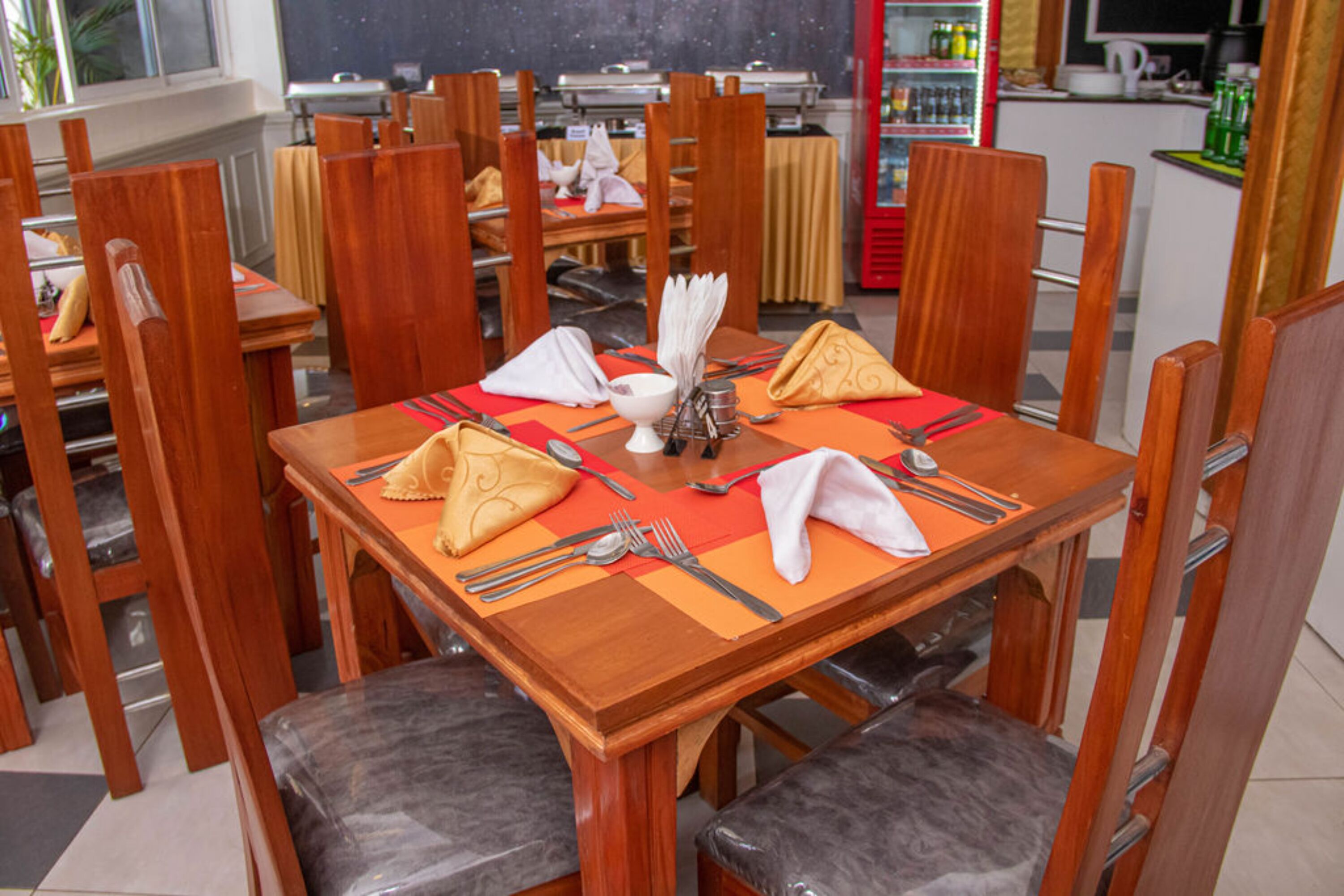 A dining area with wooden tables and chairs, equipped with cutlery and napkins.