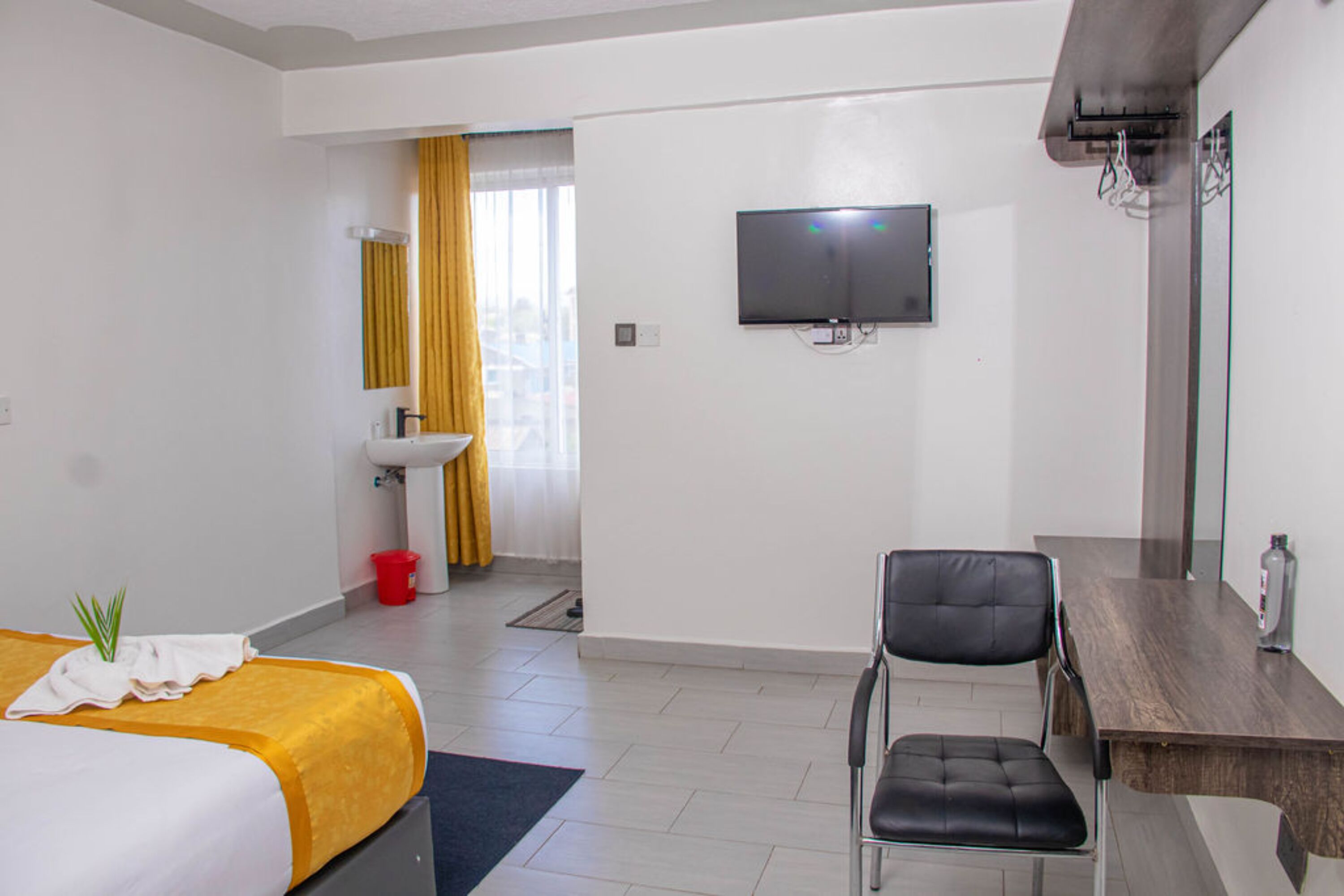 Ein Hotelzimmer mit Bett, Schreibtisch, Stuhl, Fernseher, Waschbecken und Spiegel.