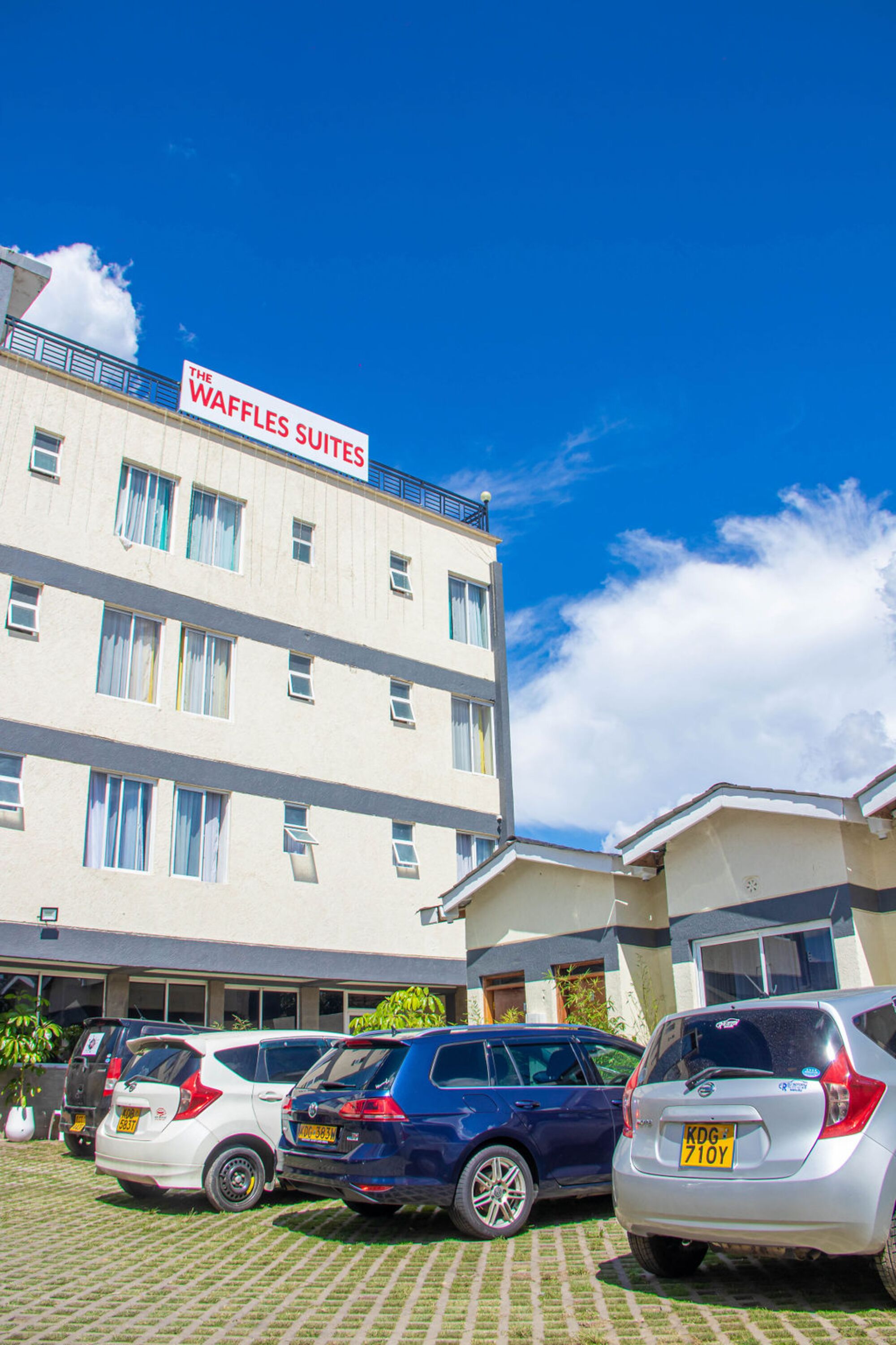 A hotel named "The Waffles Suites" with multiple floors and a parking area with several cars.