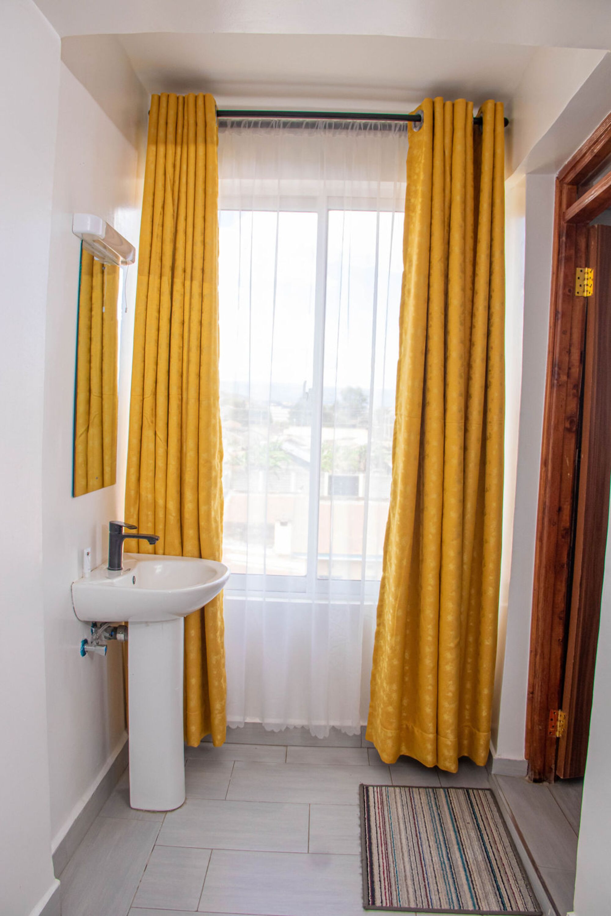 A bathroom with a white sink, yellow curtains, a window, and a wooden door.