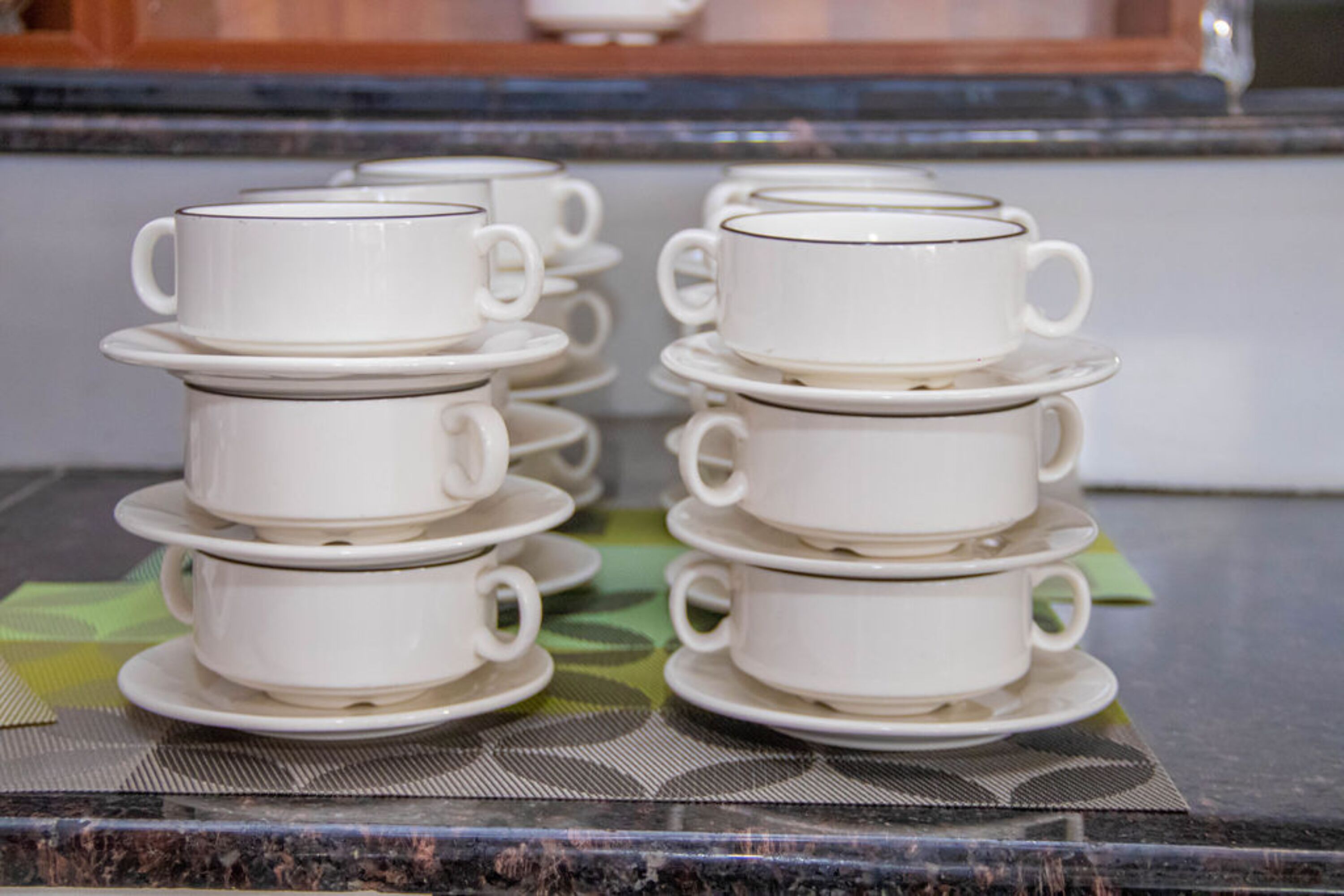 Una pila de tazas y platillos blancos sobre un tapete estampado.