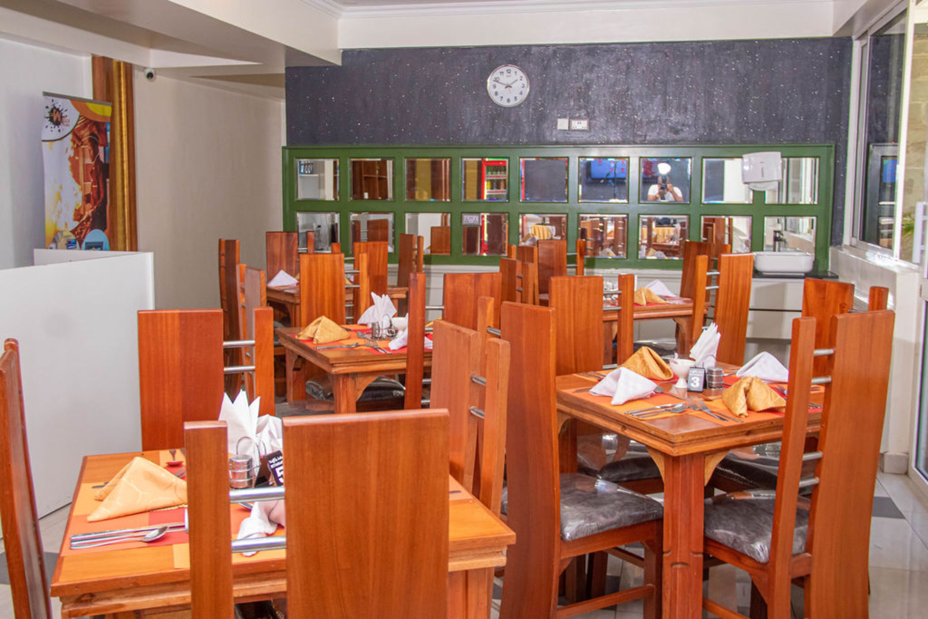 Un restaurant avec des tables et des chaises en bois, une horloge au mur et une vue sur la rue à travers les fenêtres.