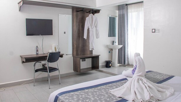 Une chambre d’hôtel comprenant un lit, un bureau, une chaise, une télévision, un peignoir et une salle de bain avec un lavabo et un miroir.