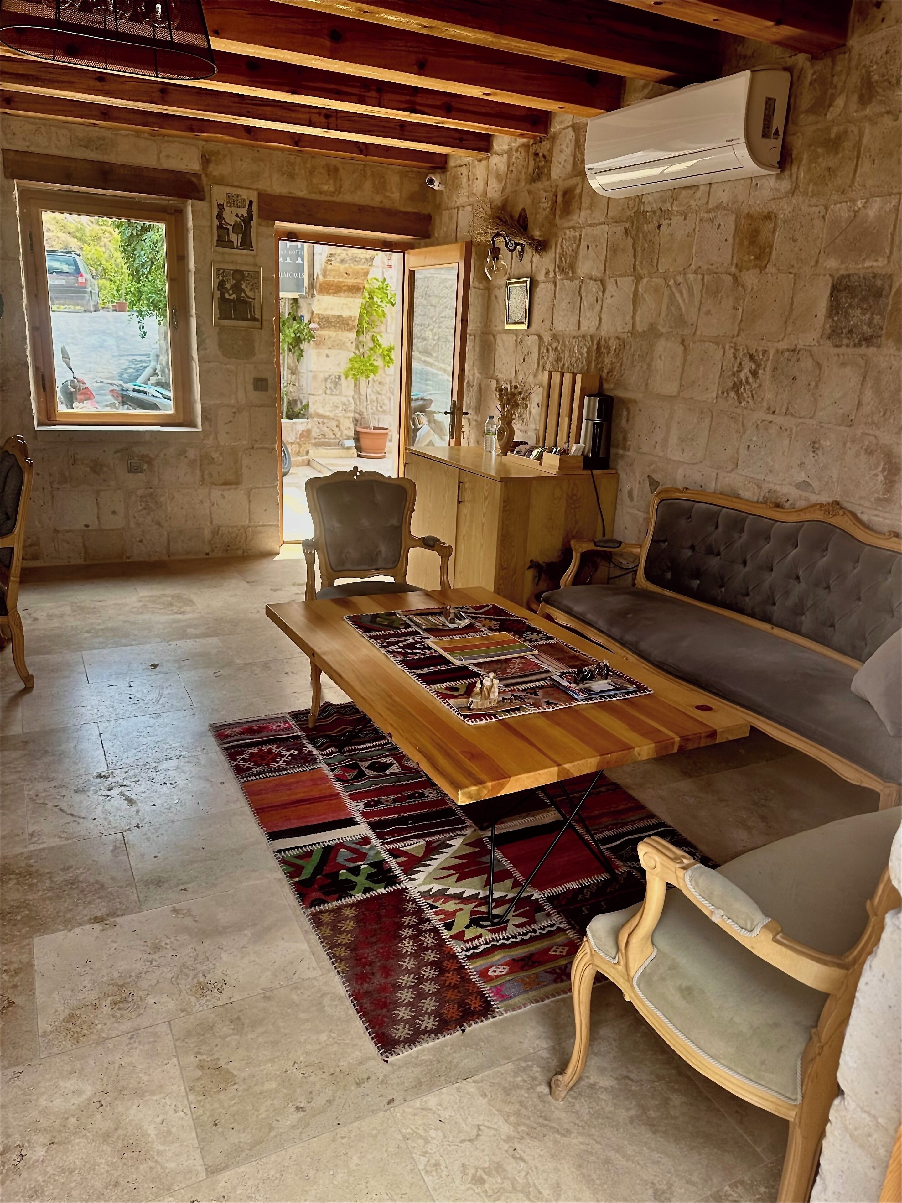 A rustic room with a stone wall, wooden furniture, a large window, and a view of the outside.