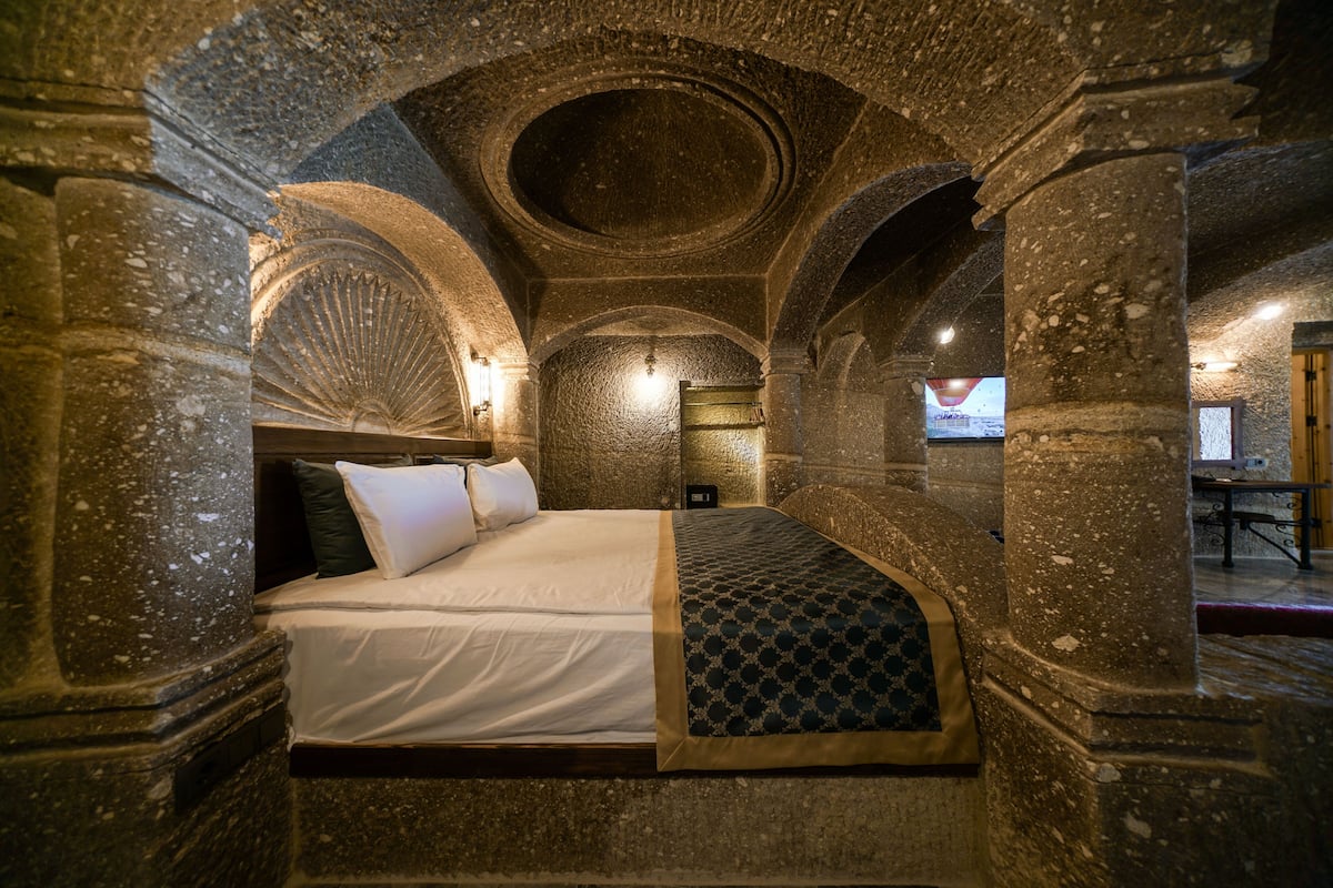 A stone-walled room with a bed, a circular skylight, and a stone bench.