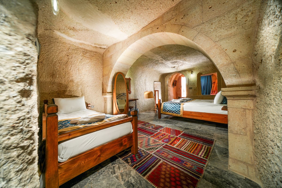 A room with two wooden beds, a patterned rug, stone walls, and an arched ceiling.