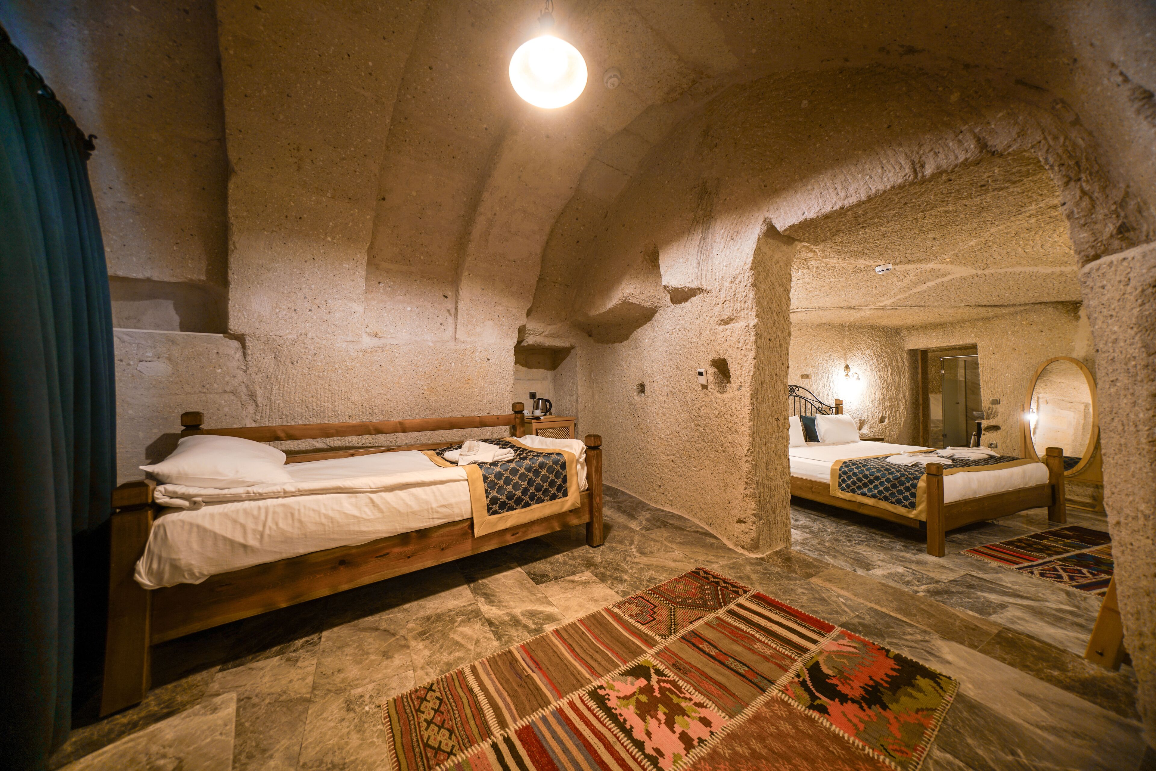 A rustic room with two wooden beds, a stone ceiling, and a large mirror.