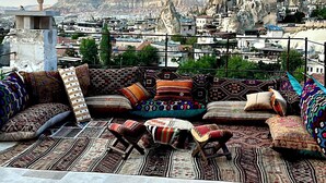 A rooftop terrace with a view of a cityscape, featuring a mix of traditional and modern architecture, and a variety of colorful textiles on the seating area. - Caverna Hotel Premium Caves (Nevsehir)