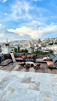 Una terraza en la azotea con vistas a un paisaje urbano, que muestra una mezcla de arquitectura tradicional y moderna, y una variedad de textiles coloridos en la zona de estar.