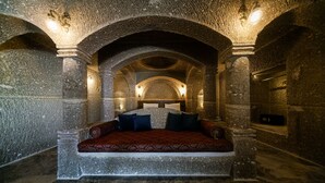 A stone-walled room with a bed under an arched ceiling, stone columns, and wall-mounted lights. - Caverna Hotel Premium Caves (Nevsehir)