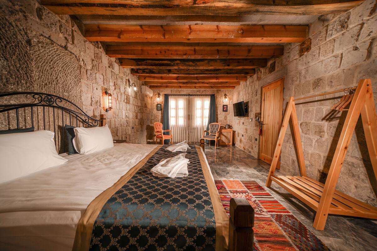 A rustic room with a bed, a wooden bench, a chair, and a television.