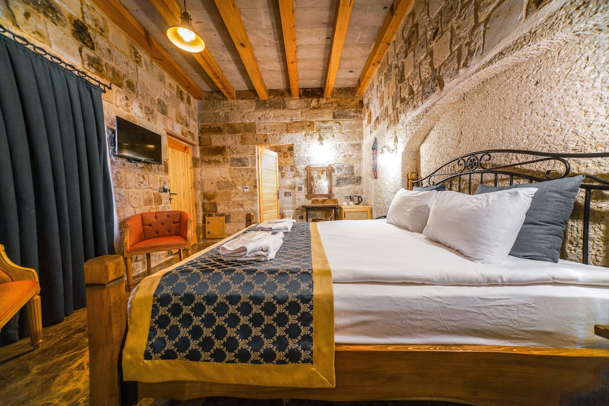 A bedroom with a wooden bed, a chair, a television, and stone walls.