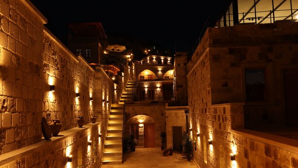 A narrow stone corridor with a staircase leading to an upper level, illuminated by warm lighting. - Caverna Hotel Premium Caves (Nevsehir)