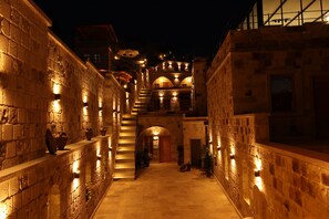Un estrecho pasillo de piedra con una escalera que conduce a un nivel superior, iluminado por una cálida luz.